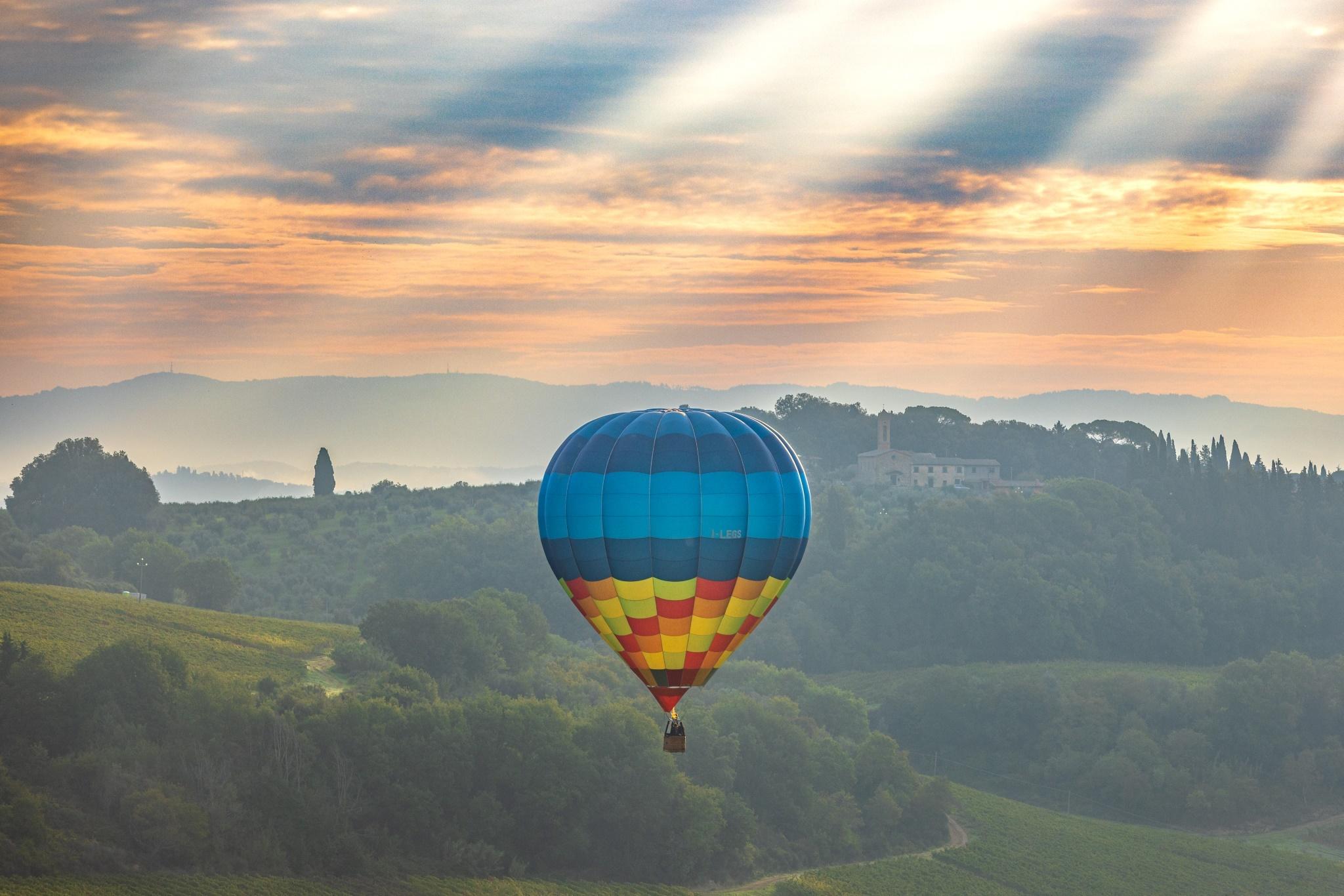 A hot air balloon flying above the hills of Tuscany during sunrise.