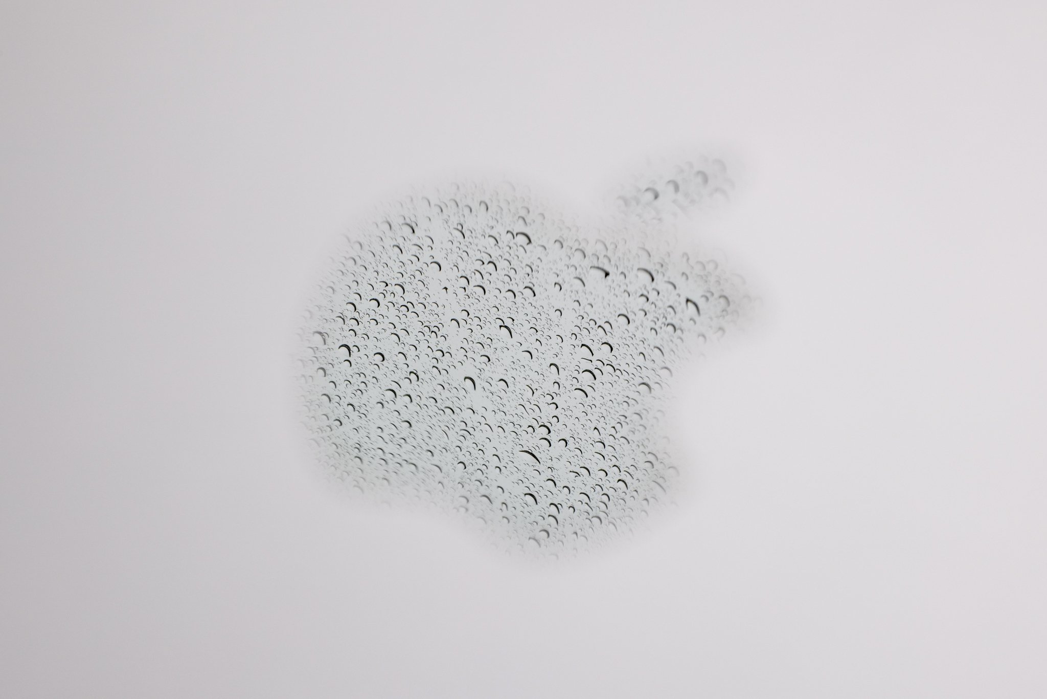 A reflection of rain in the Apple logo on a laptop photographed at f/14