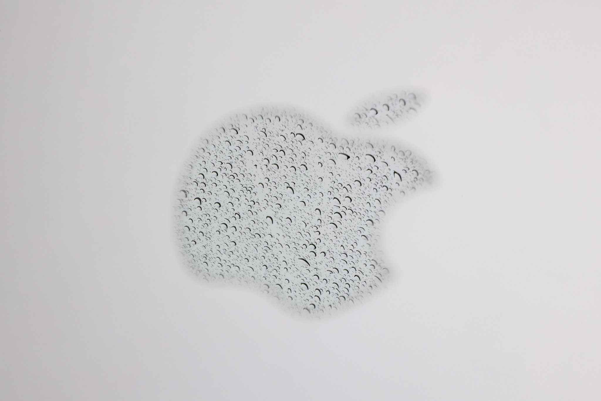 A reflection of rain in the Apple logo on a laptop photographed at f/25