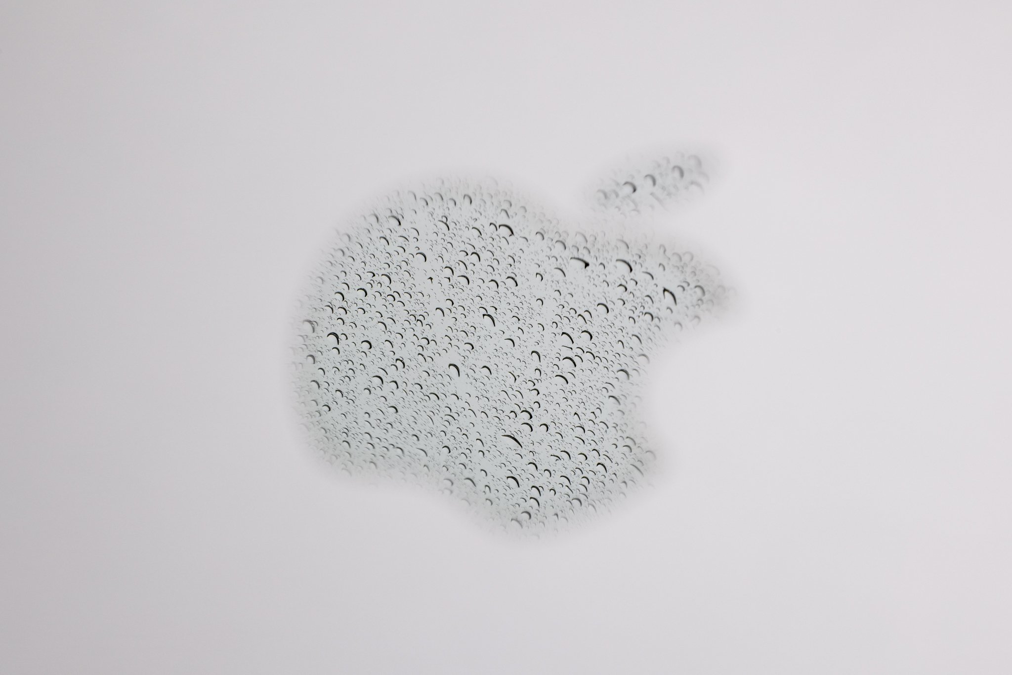 A reflection of rain in the Apple logo on a laptop photographed at f/18