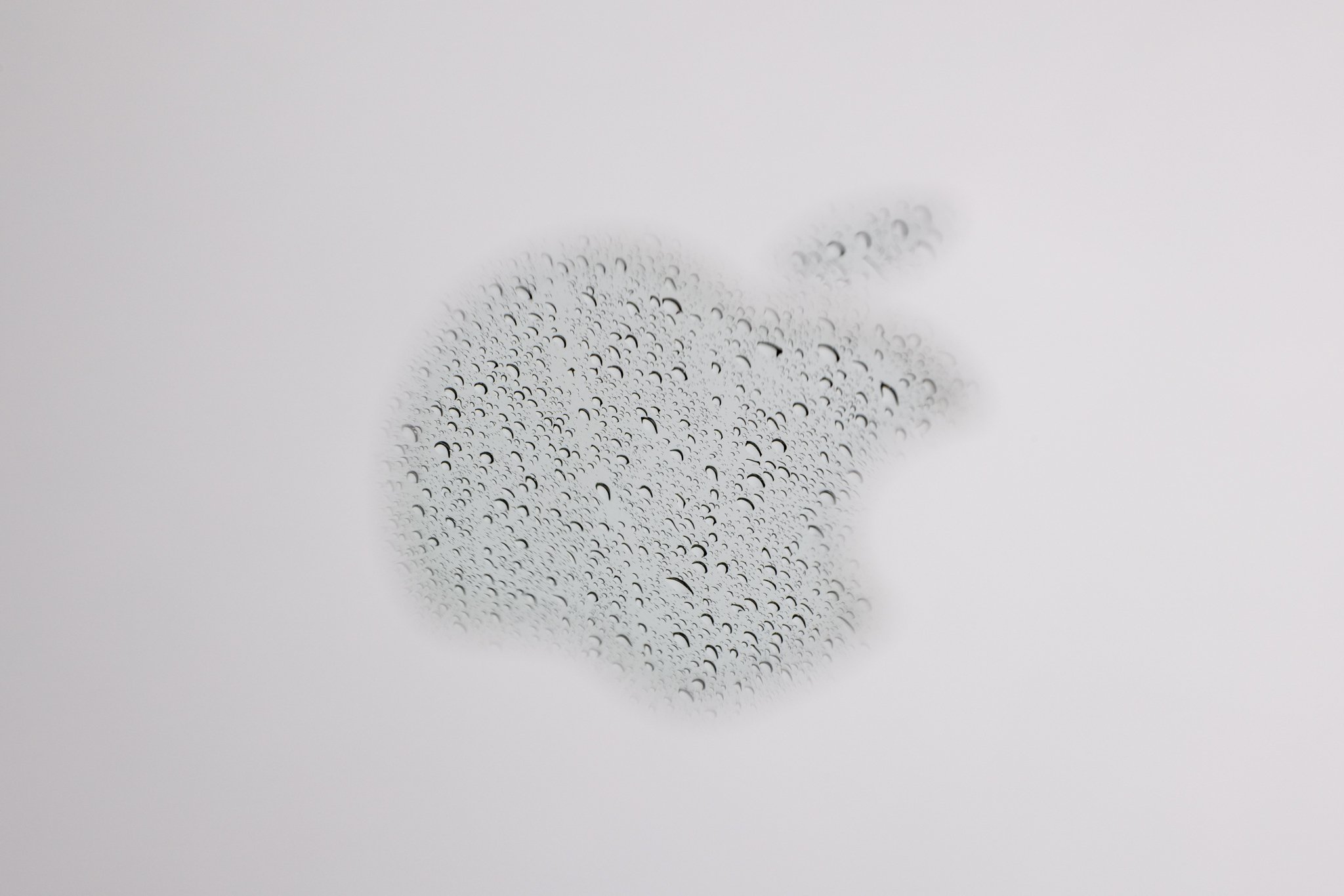 A reflection of rain in the Apple logo on a laptop photographed at f/16