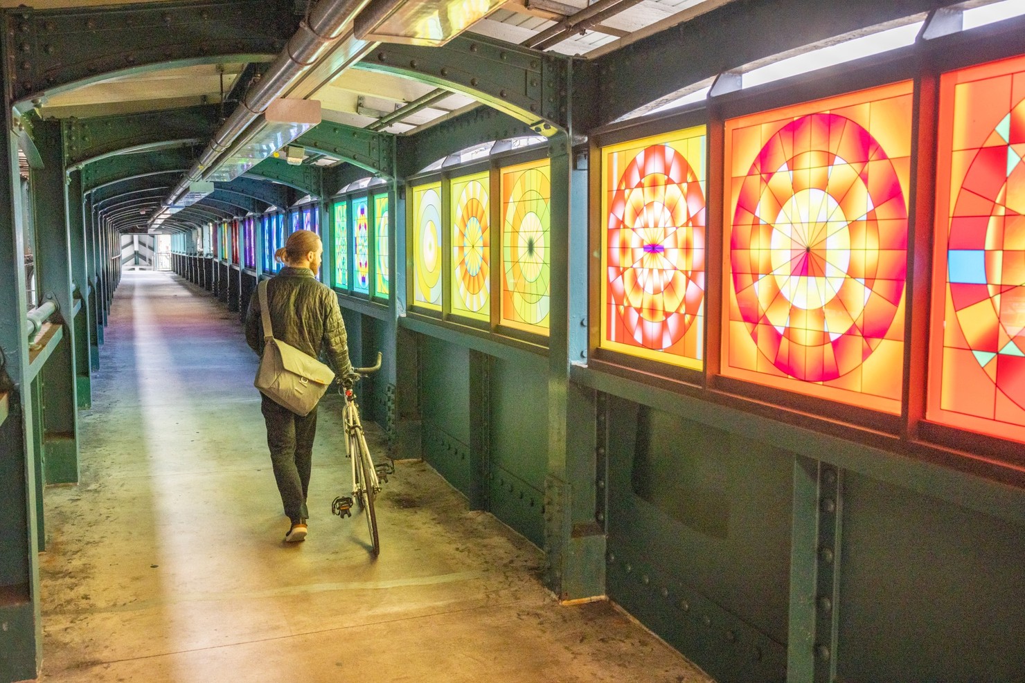 A person walking away from the camera in a tunnel of rainbow light.