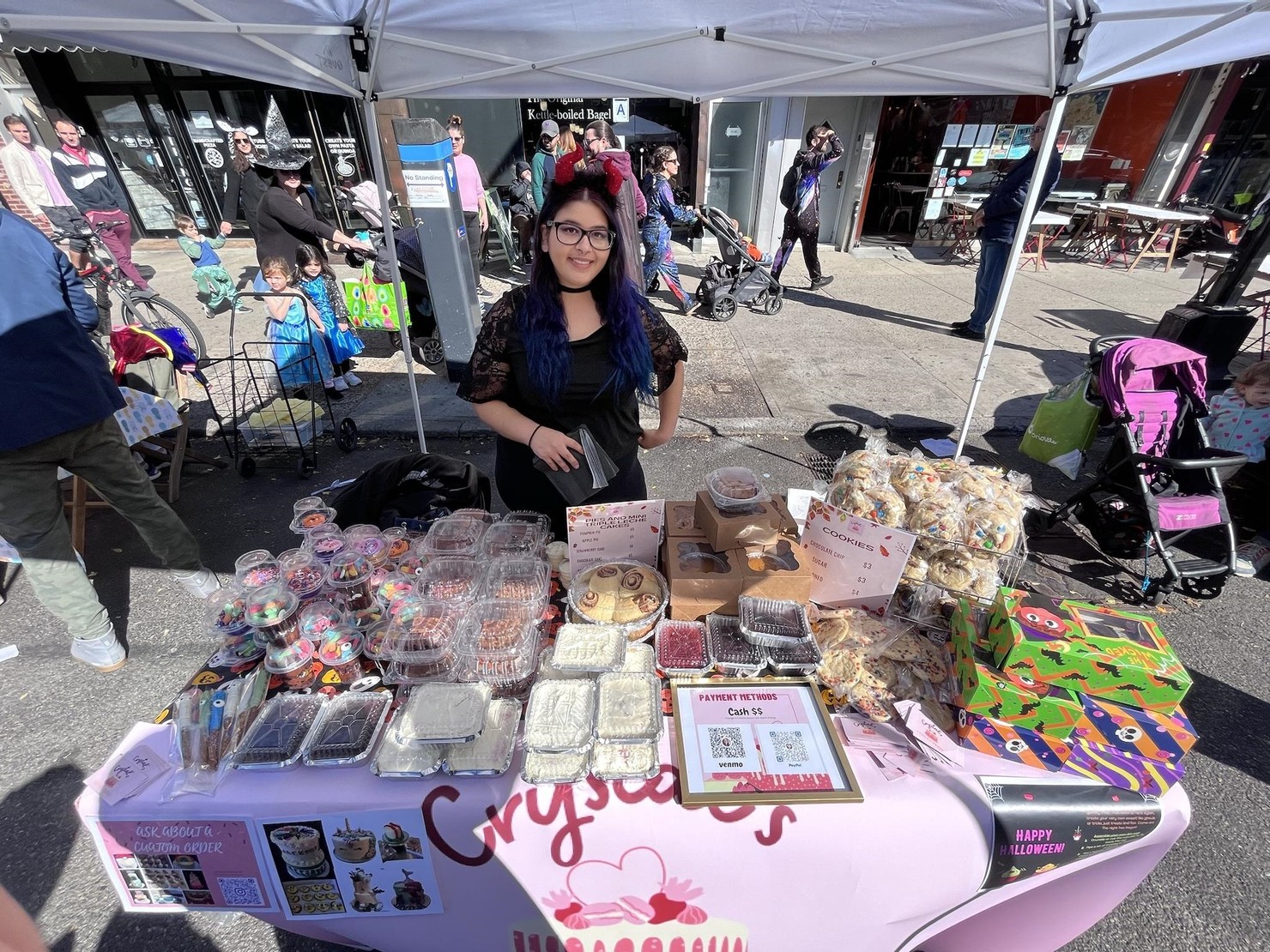 A smiling person standing at a table of baked goods.