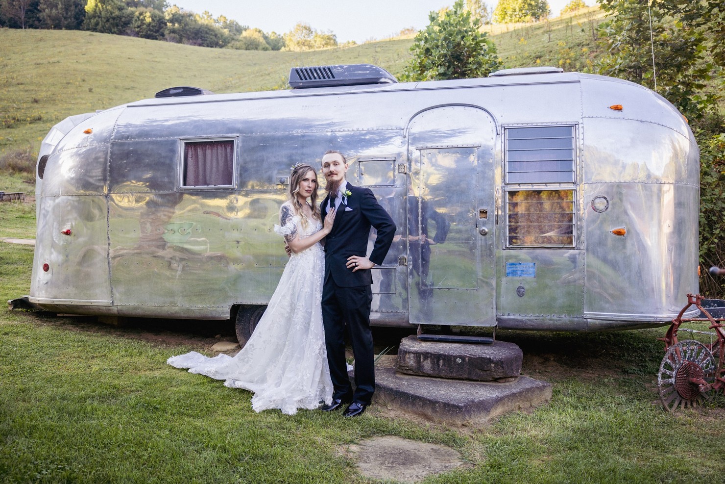 A bride and groom in wedding attire posing in front of vintage Airstream.