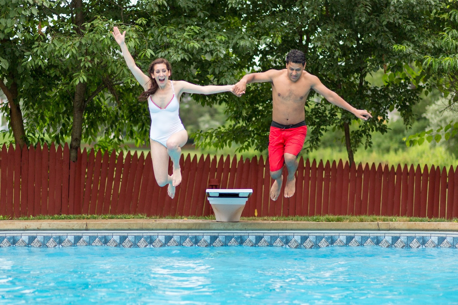 A bride and groom jumping into a swimming pool.