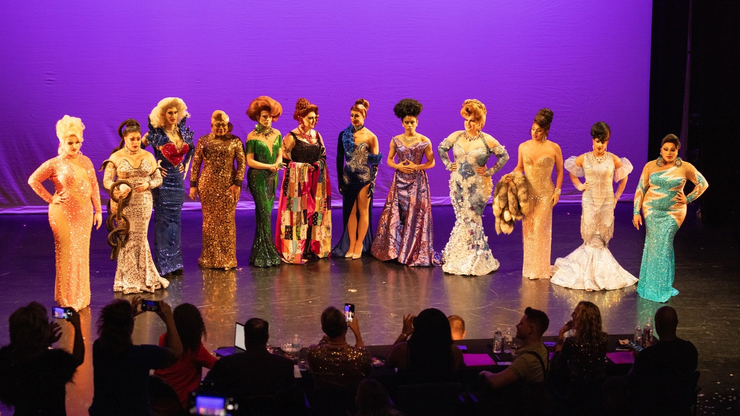 A group of drag queens standing on a stage in their fanciest eveningwear.