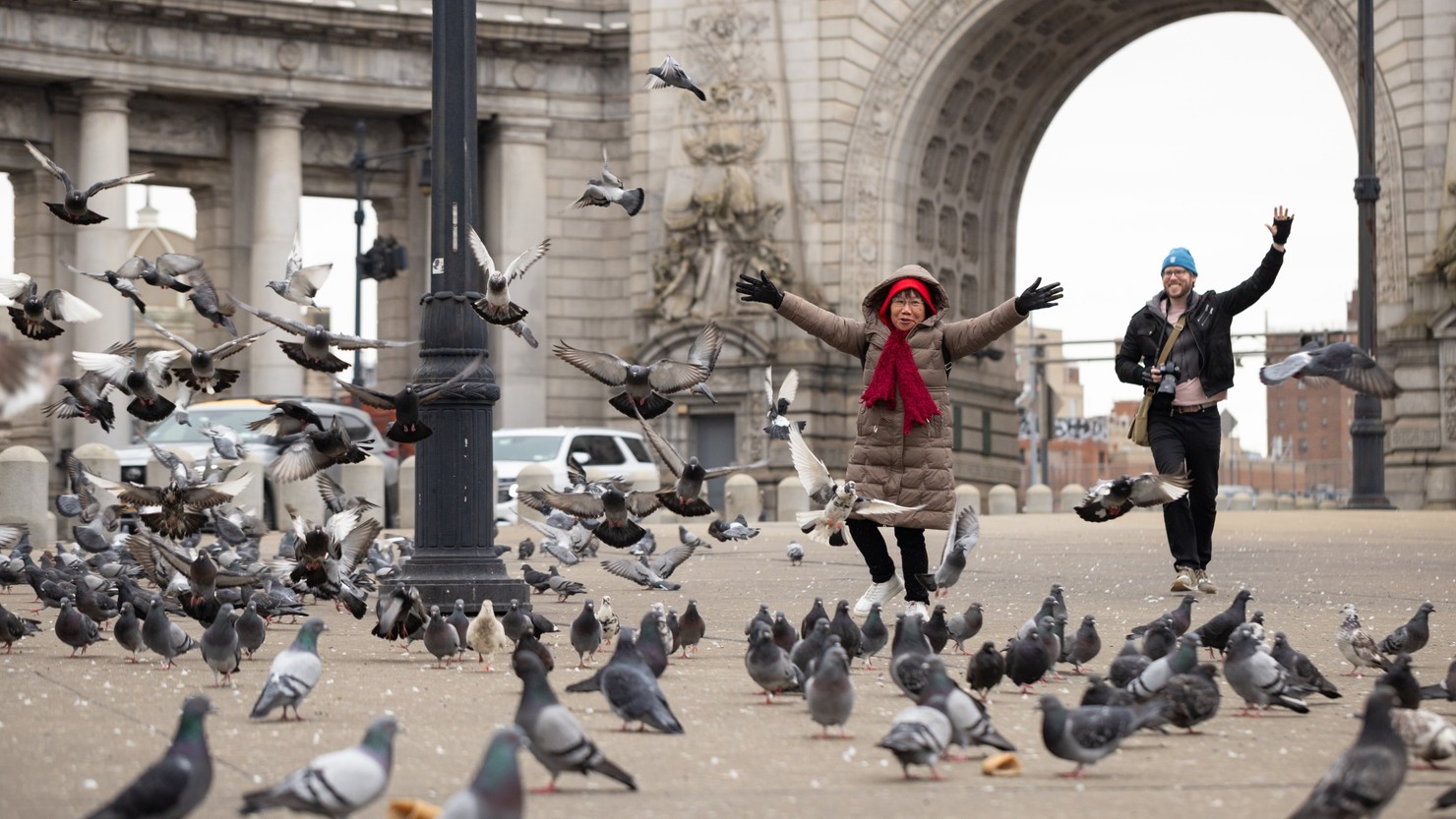 Two people running towards a group of hundreds of pigeons.
