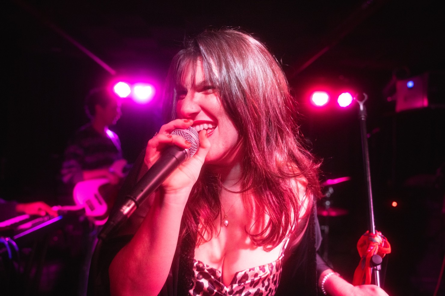 A woman leaning forward and singing into a microphone while magenta lights shine upon her.