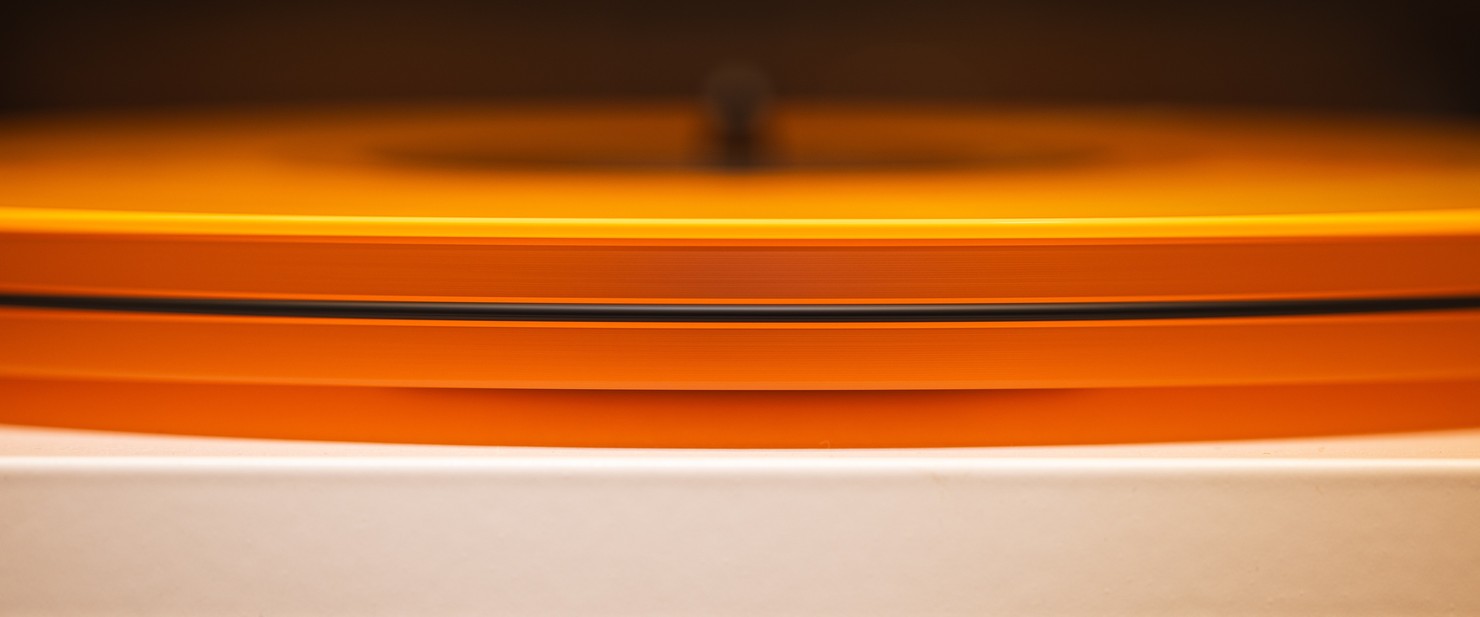 A bright orange vinyl record sitting on a clear acrylic turntable.