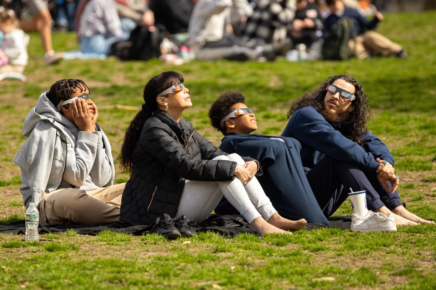 Four people wearing eclipse safety glasses, three of whom are looking up at the sun.