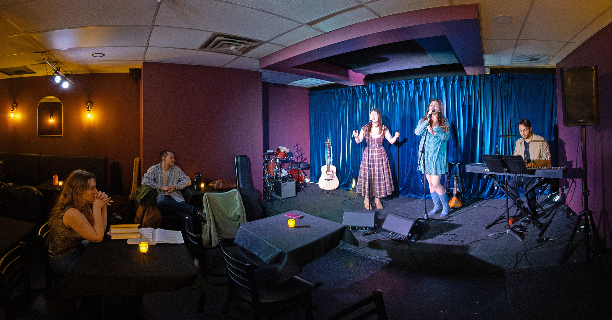 Two people are singing on a stage, one person is playing piano on a stage, and several people are listening in the audience during rehearsal for Ava Delaney's show.