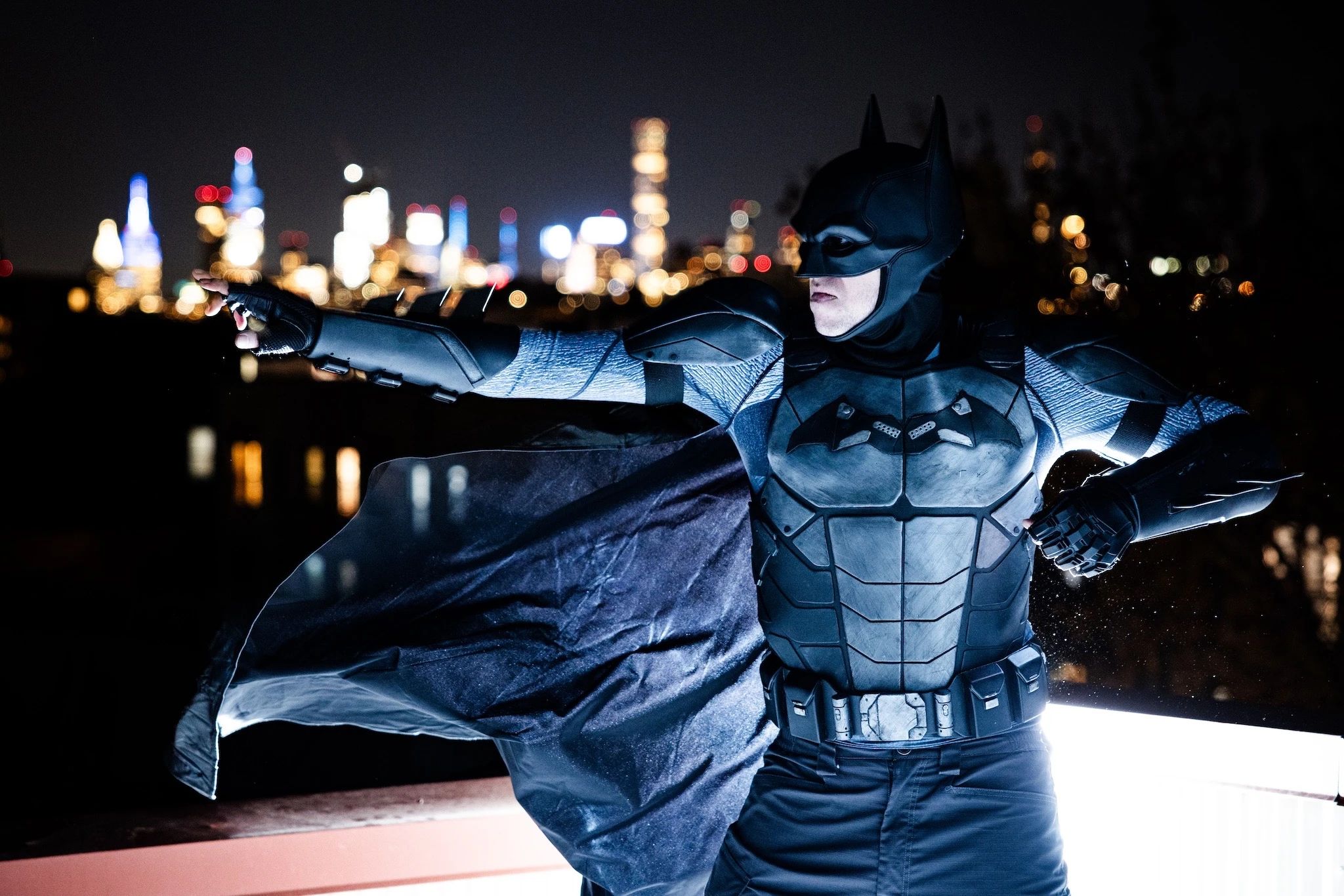 Batman posing in front of the NYC skyline, cape aloft.