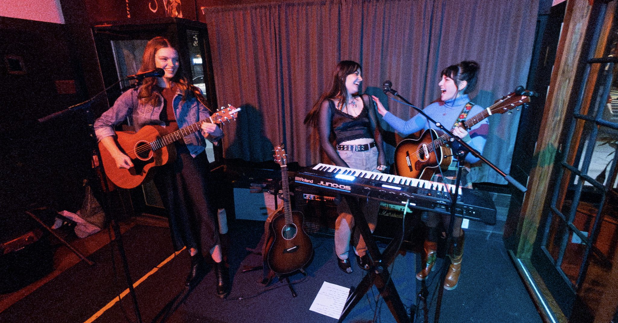 Blair Lamb is playing a guitar and singing. Two other people are playing to her left.