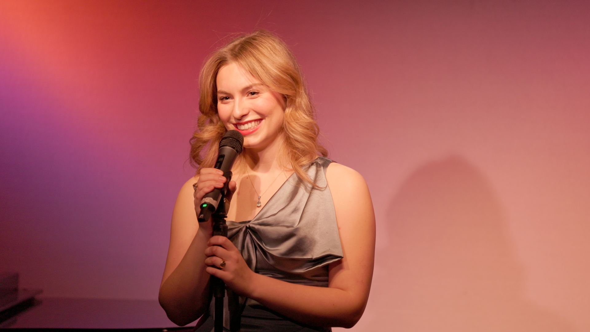 Catherine Berdie is holding a microphone and smiling.