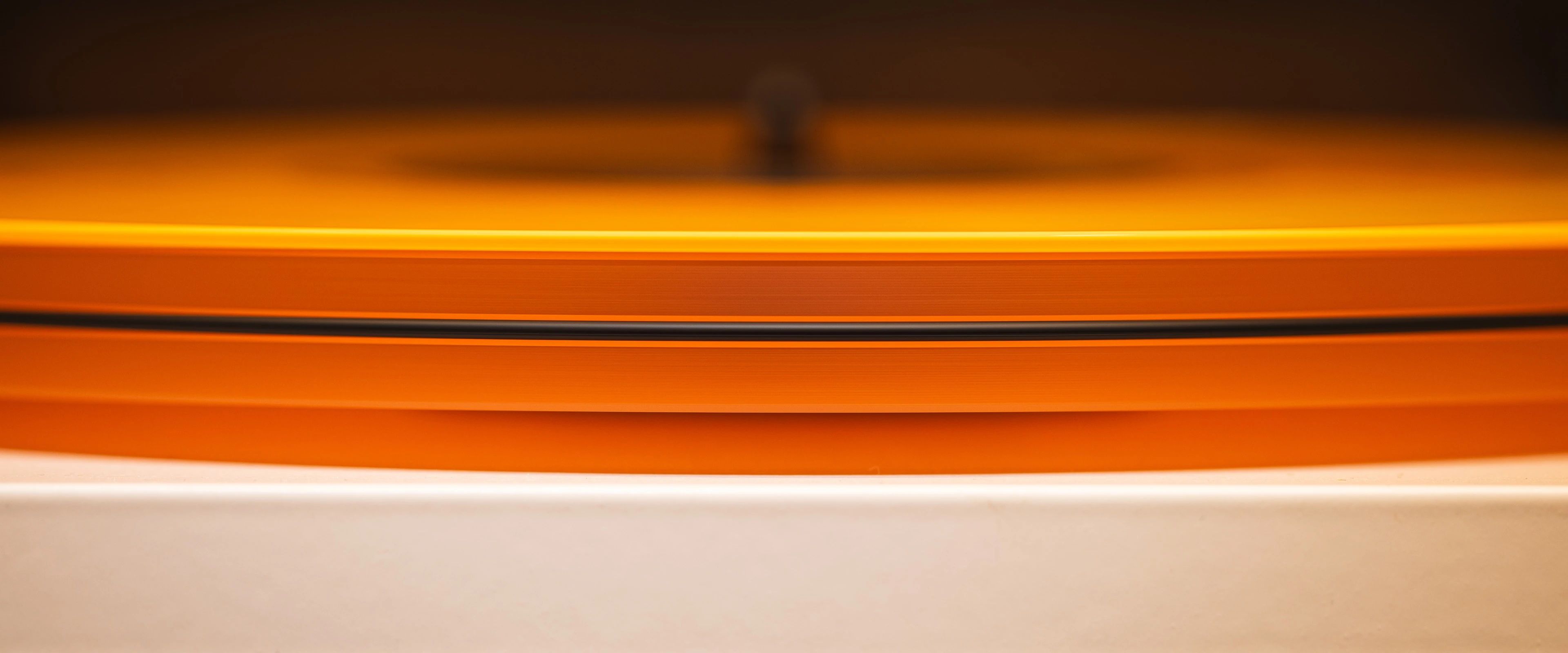 A bright orange vinyl record sitting on a clear acrylic turntable.