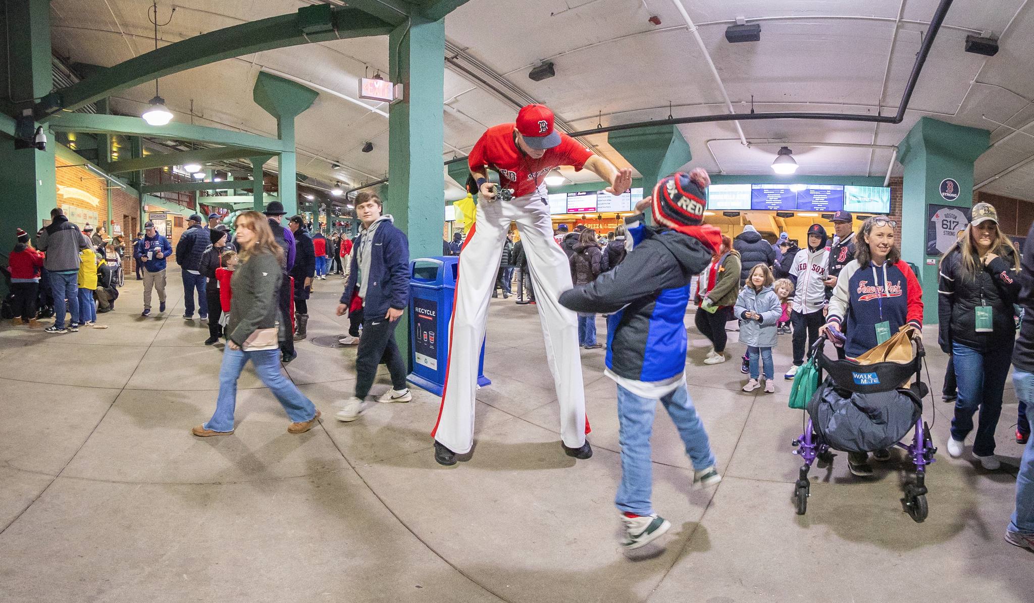 A kid jumping to high-five a man on stilts wearing a Red Sox outfit.