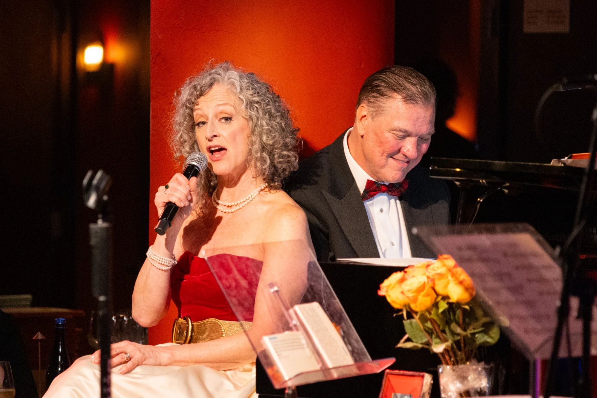 A woman singing into a microphone and a man playing the piano.