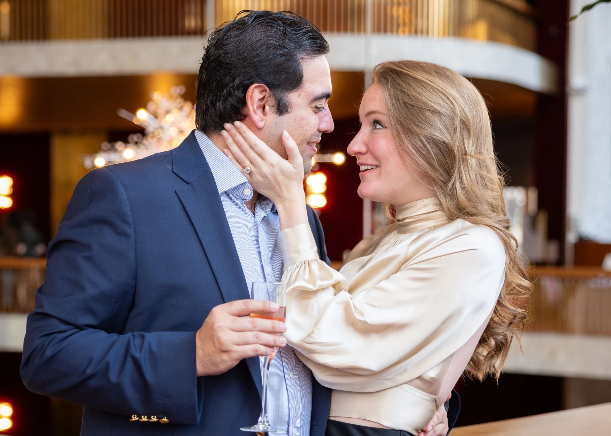 A man and a woman looking at each other lovingly. They are smiling. The woman has a new engagement ring on her finger.