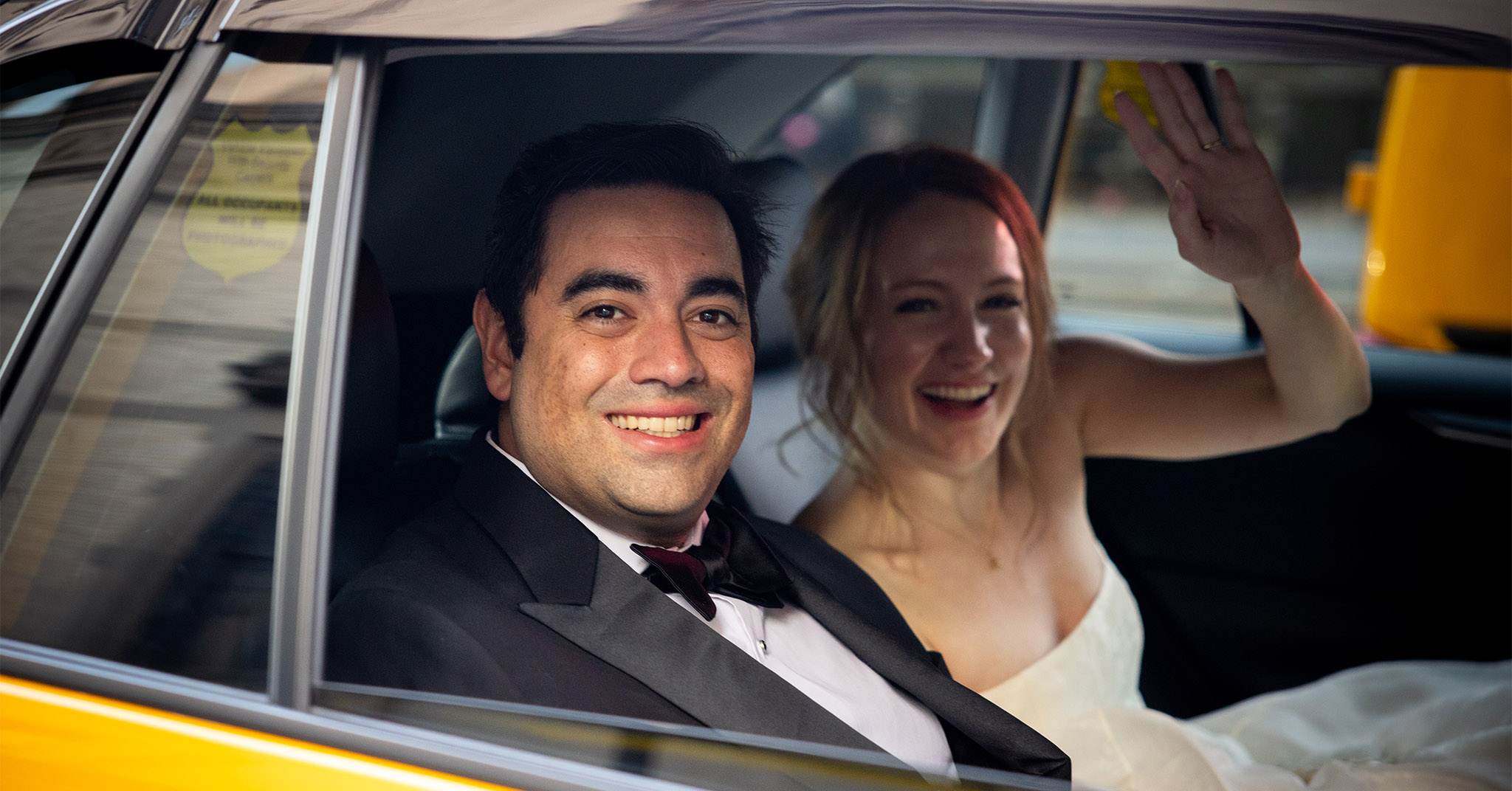 A man and a woman sitting in a NYC yellow cab, smiling.