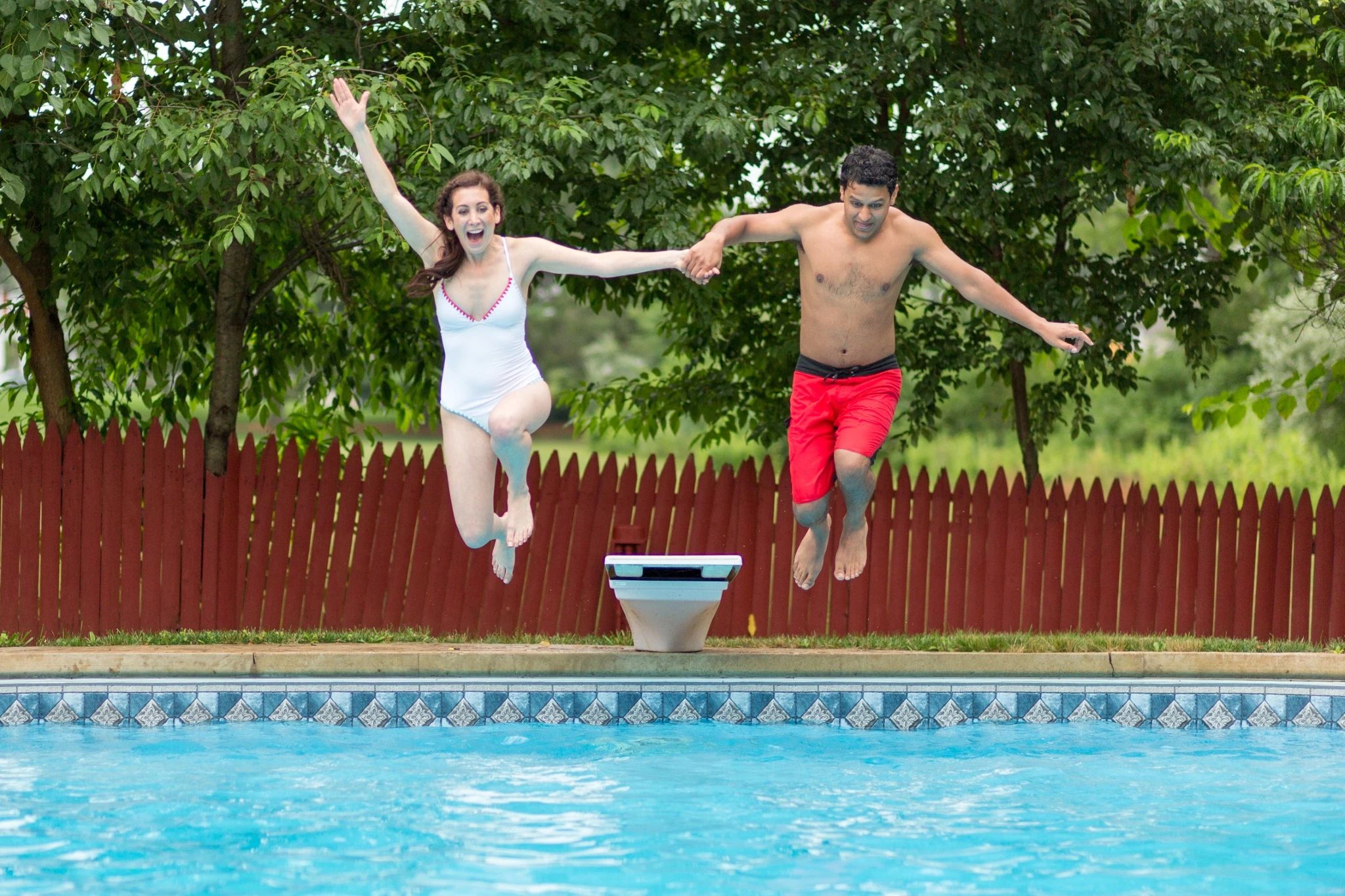 A bride and groom jumping into a swimming pool.