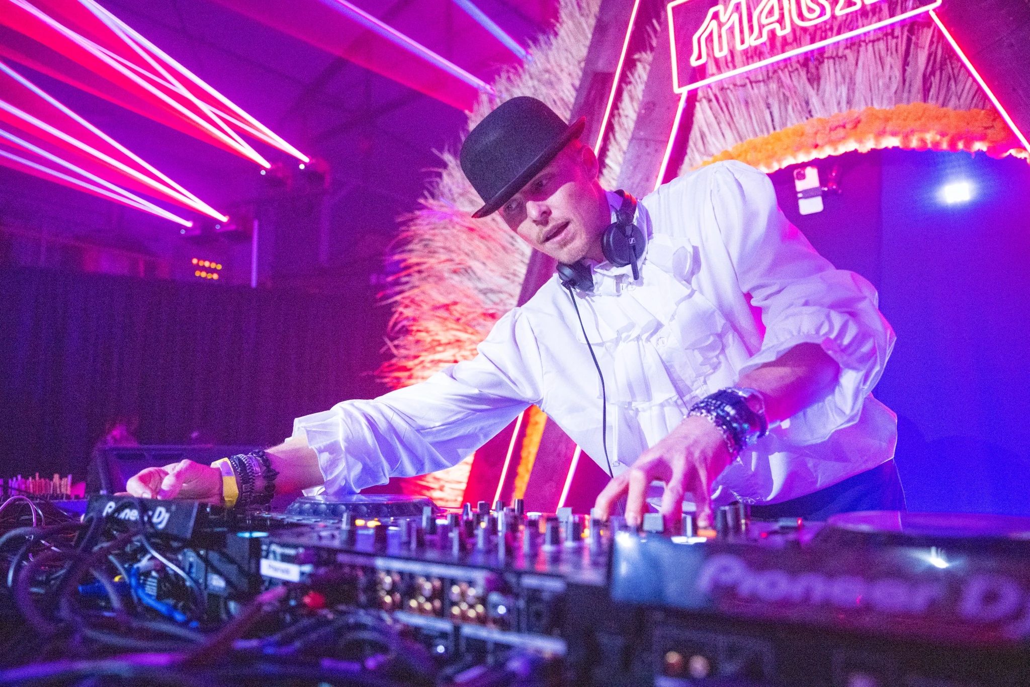 A DJ reaching across his decks to modify the music.