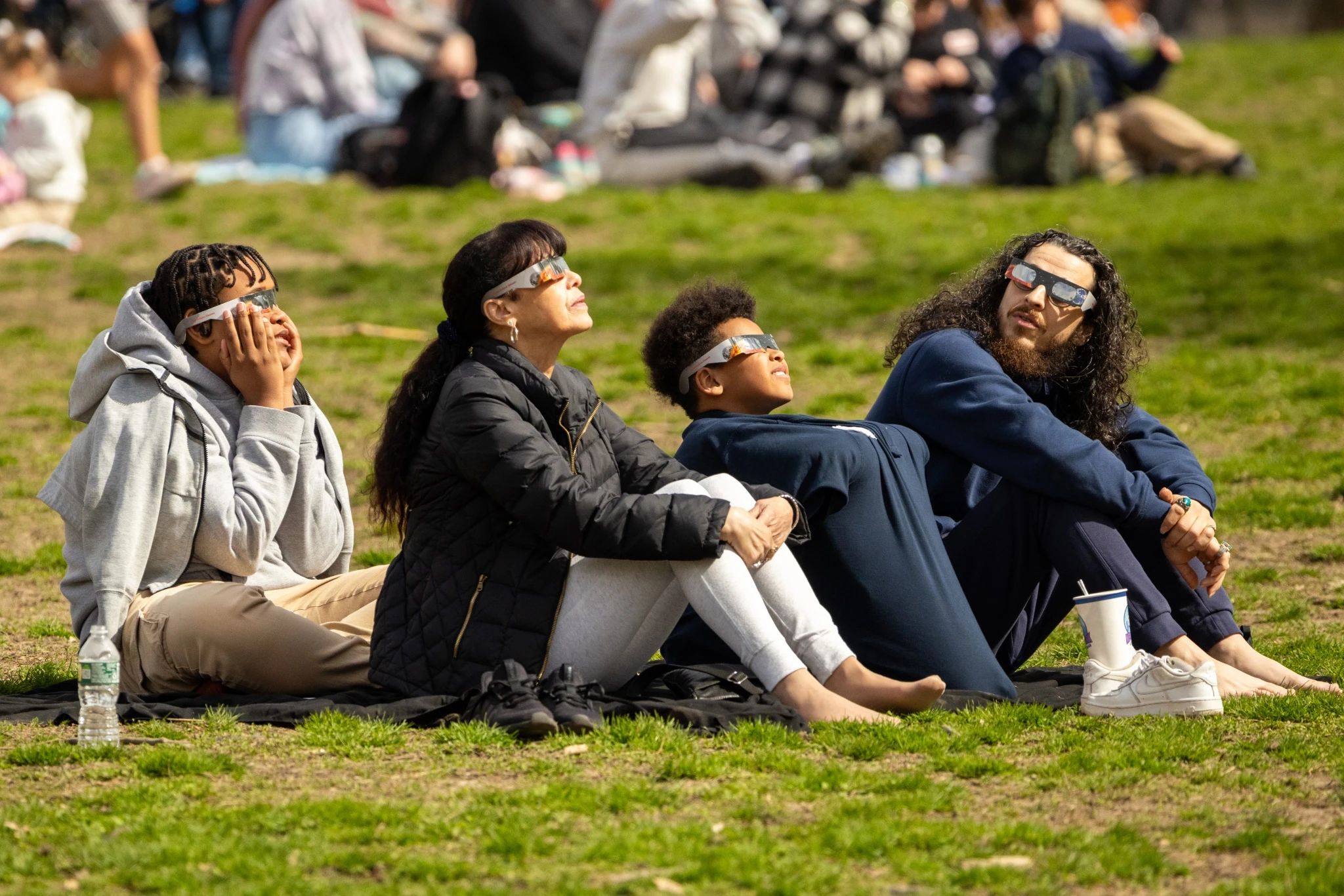 Four people wearing eclipse safety glasses, three of whom are looking up at the sun.