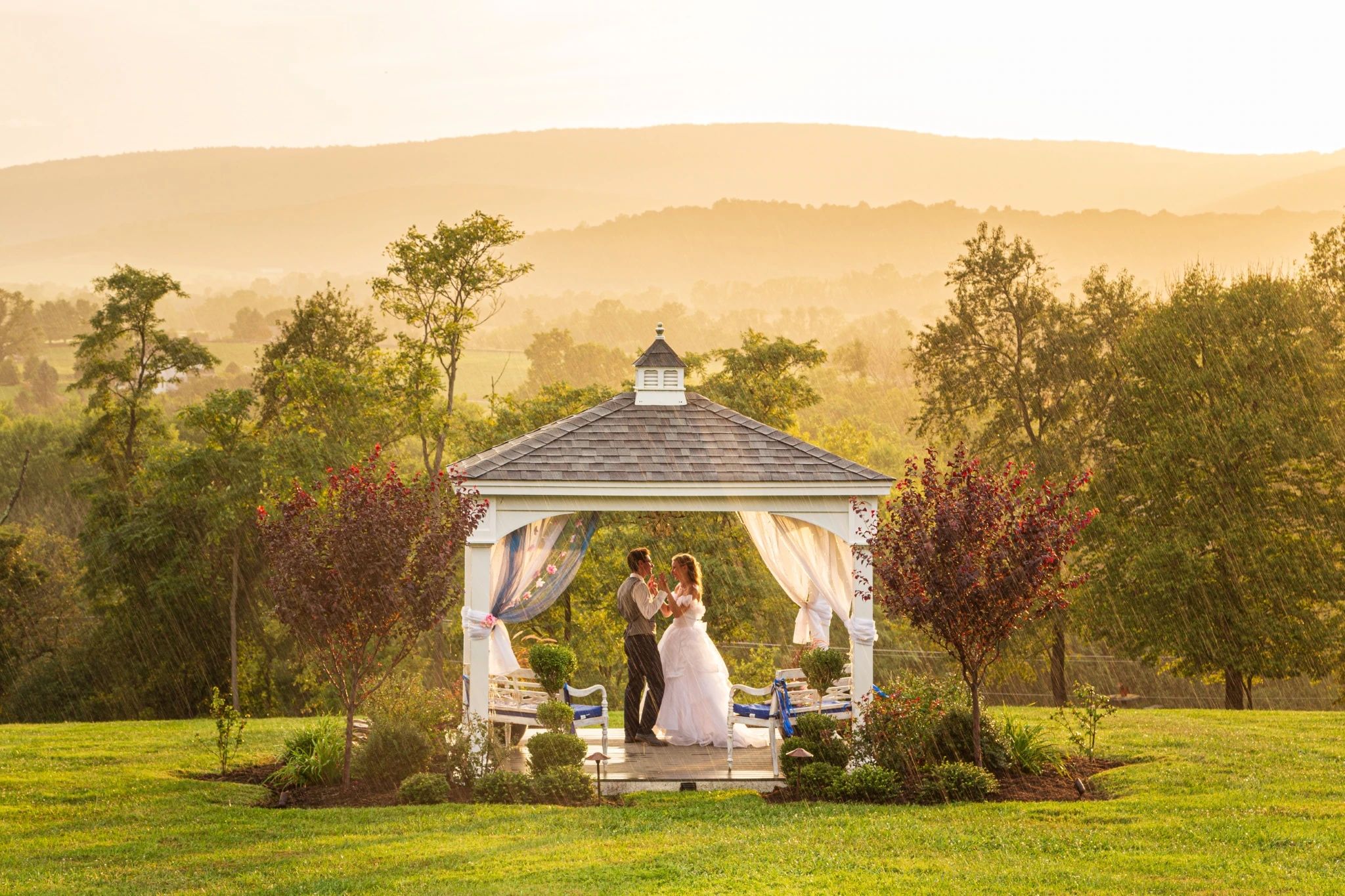 A smiling wedding couple standing in a gazebo at sunset. It is raining lightly