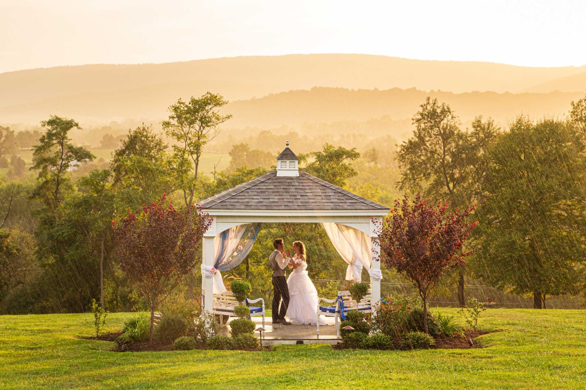 A smiling wedding couple standing in a gazebo at sunset. It is raining lightly.